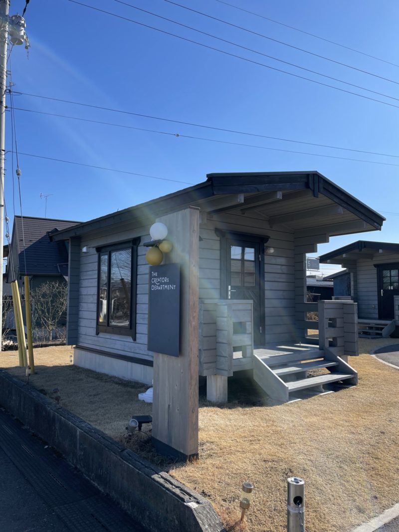 宝積寺駅東口にあるクリエイターズデパートメント5号棟の外観。ログハウス風の小さなお店が青空の下に建っている