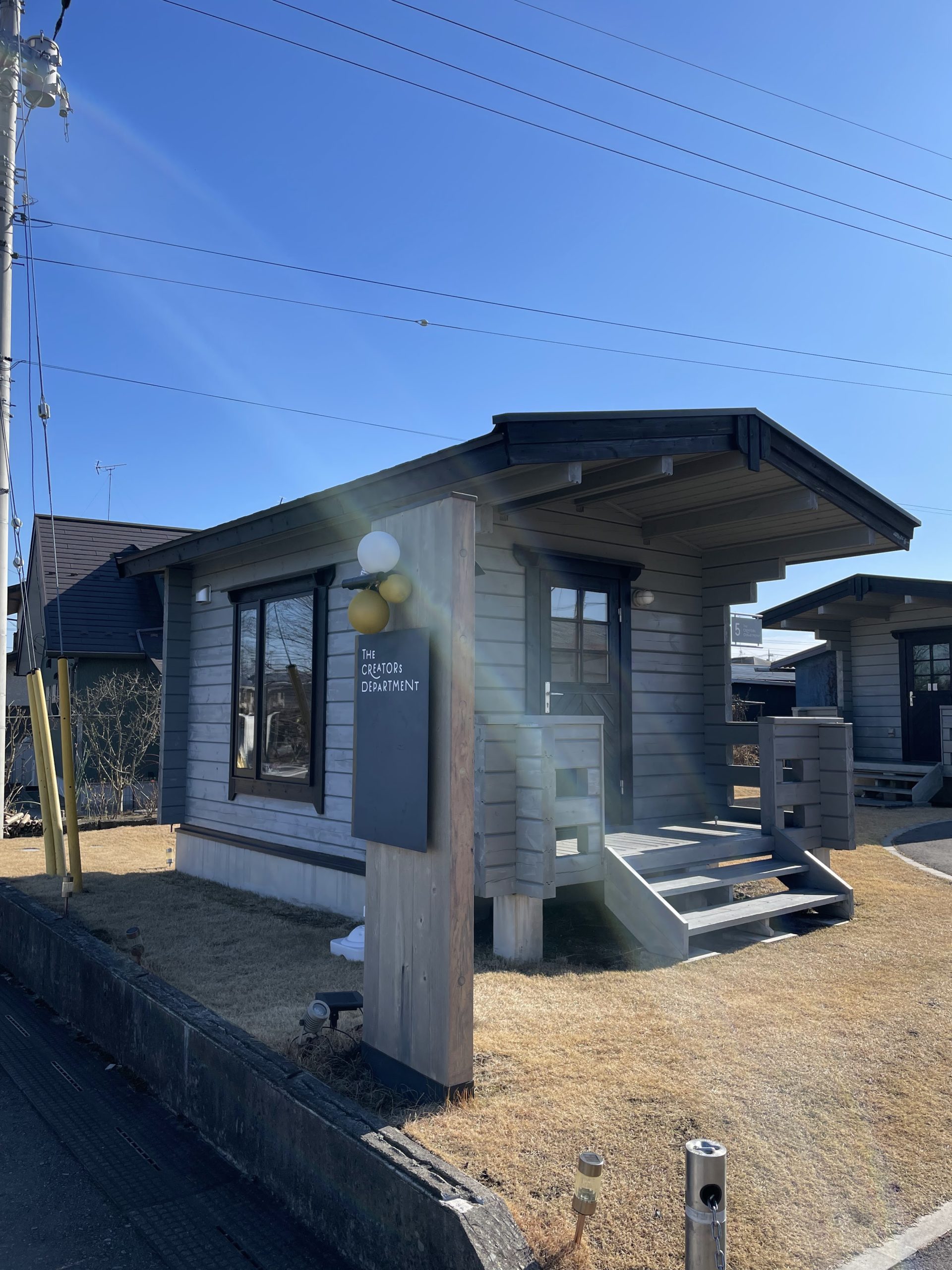 宝積寺駅東口にあるクリエイターズデパートメント5号棟の外観。ログハウス風の小さなお店が青空の下に建っている